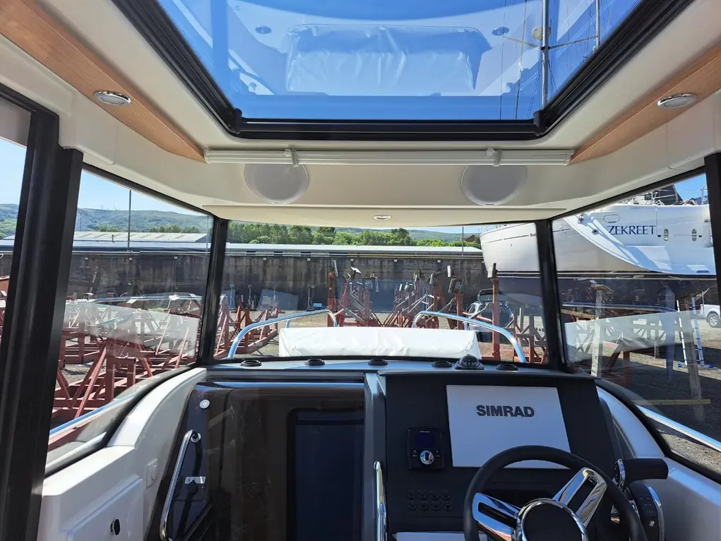 Interior view of a modern boat dashboard featuring a SIMRAD display, steering wheel, and a panoramic glass roof.